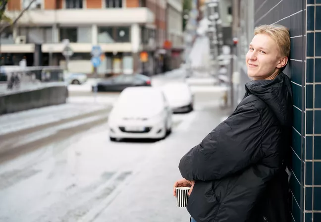 Emil står utomhus med ryggen mot en vägg. Det är snö ute.  